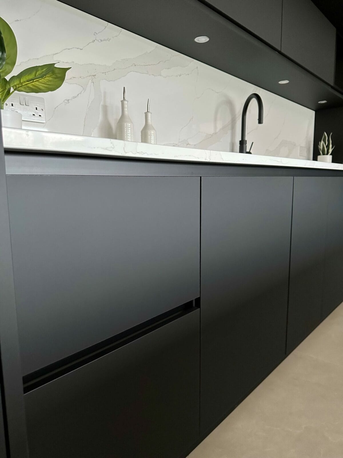 Black handleless kitchen showing use of stone quooker tap and lighting